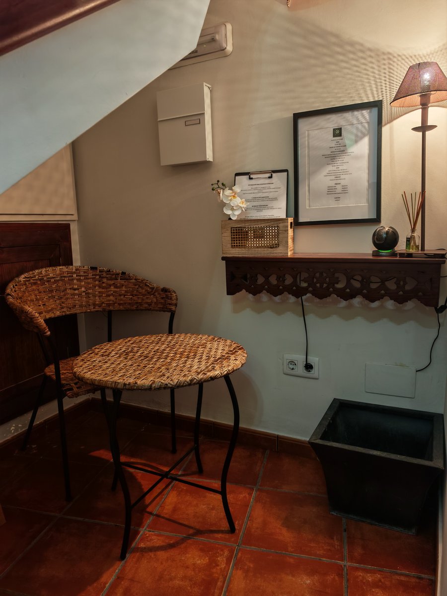 El hall de entrada de la casa: la mesa y la silla de mimbre junto a la estantería de madera con la lámpara encendida